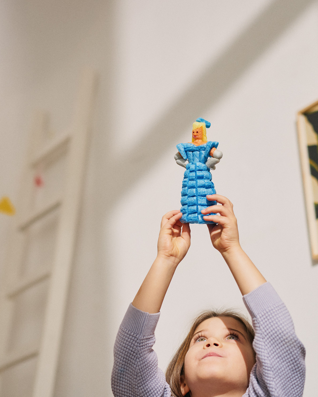 Ein Kind hält eine Figur aus blauen Nubsis in die Luft, die wie eine Person in einem Kleid aussieht.