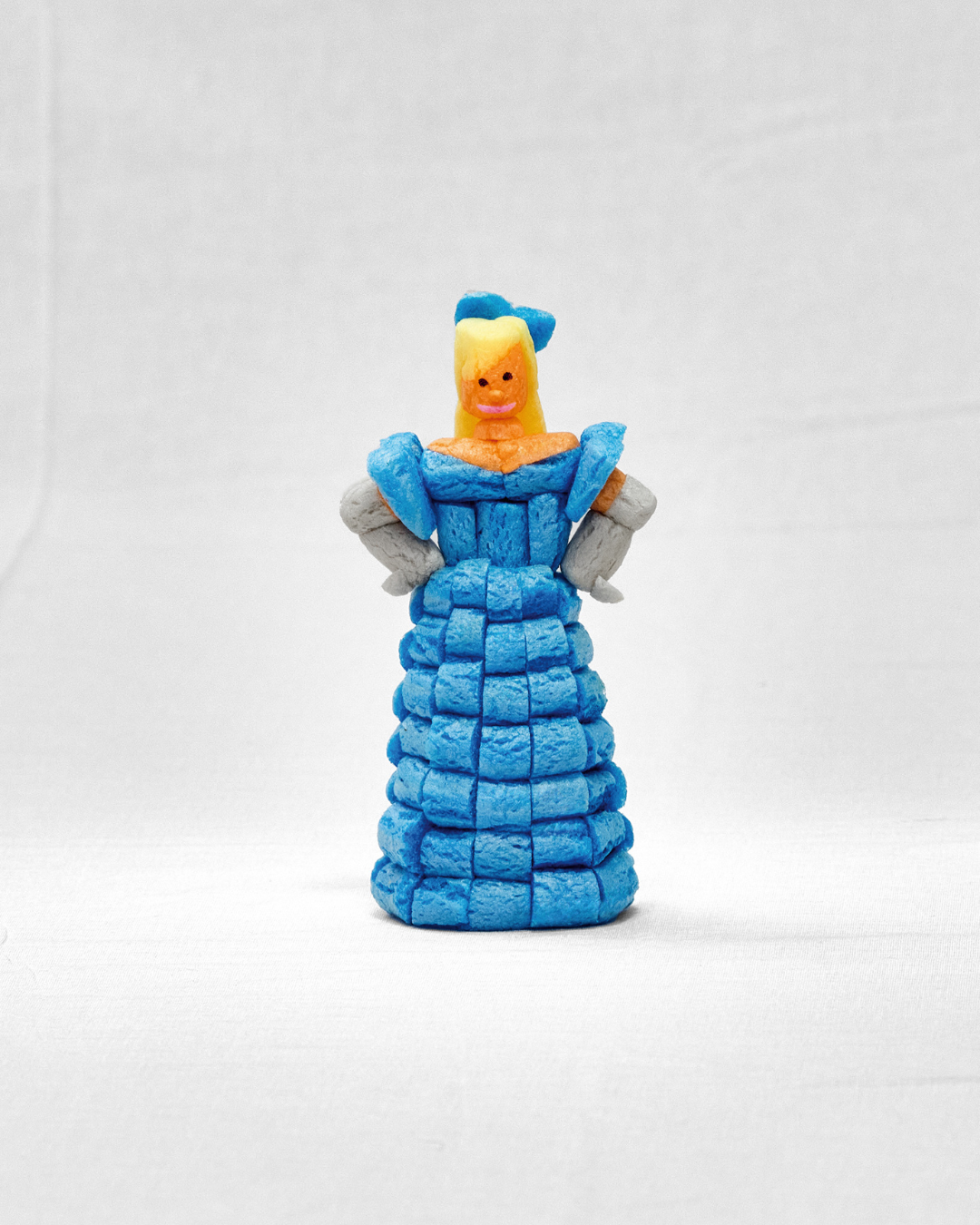 Eine Figur aus blauen, grauen und orangen "Nubsis", die eine Frau in einem Kleid darstellt, vor weißem Hintergrund.
