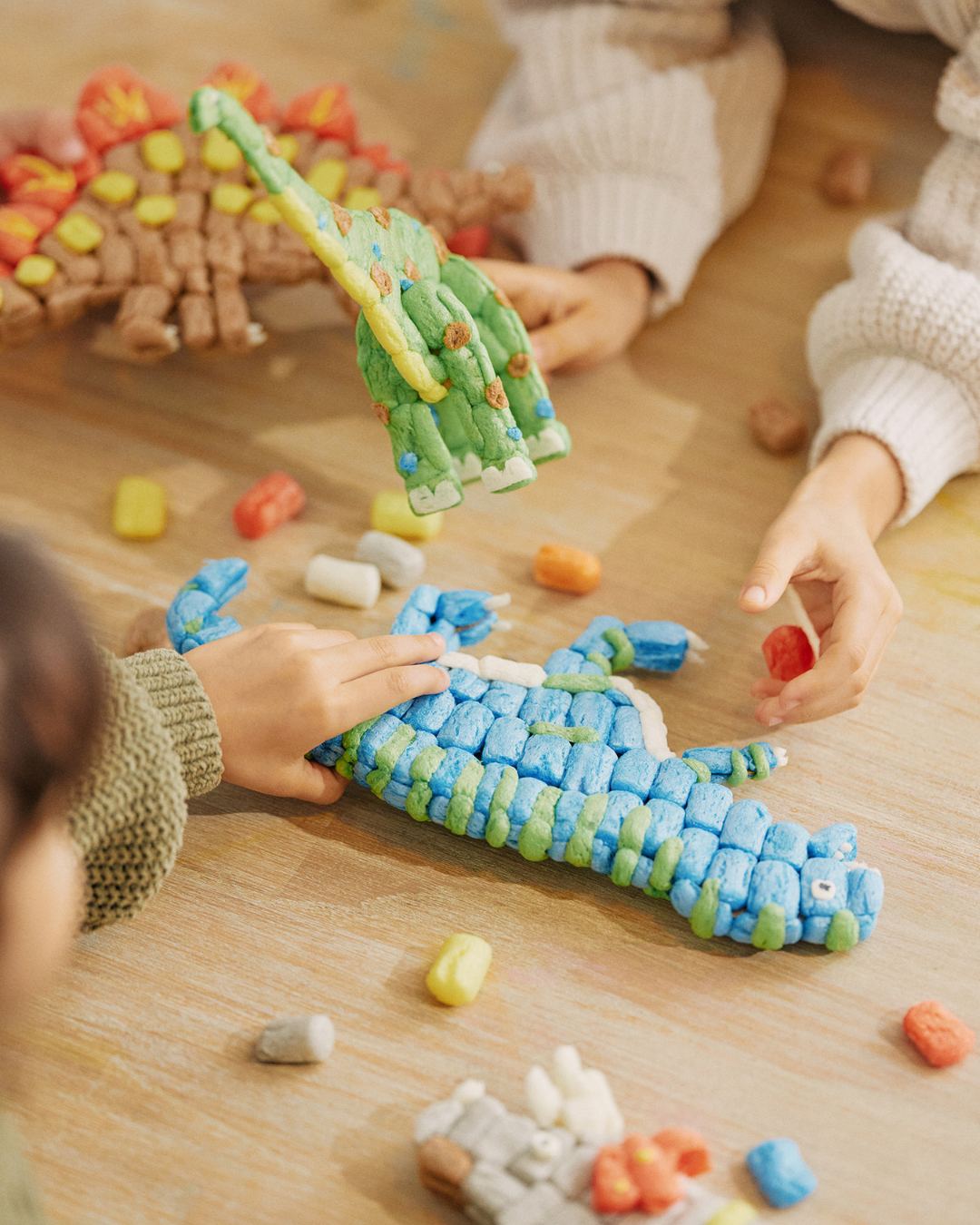 Kinder bauen Dinosaurierfiguren aus bunten Nubsis auf einem Tisch.