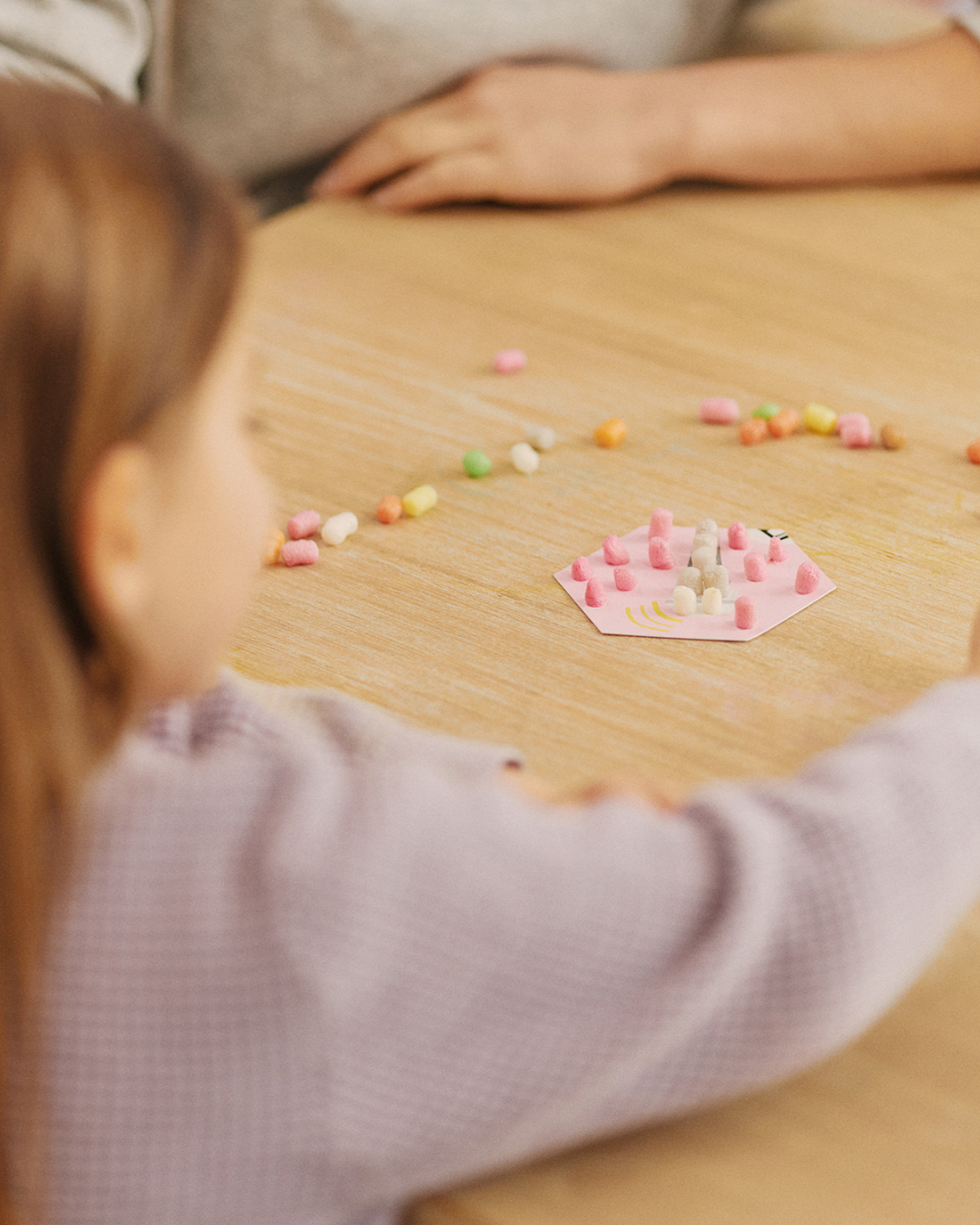 Ein Kind spielt mit bunten Nubsis auf einem Tisch. Im Hintergrund ist ein Erwachsener zu sehen.