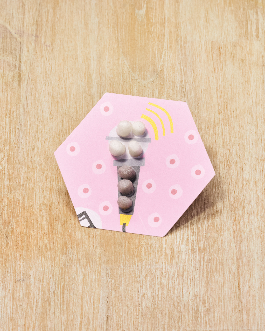 Sechseckige pinke Karte mit Kreisen, darauf kleben weiße und braune Nubsis, auf einem Holztisch liegend.
