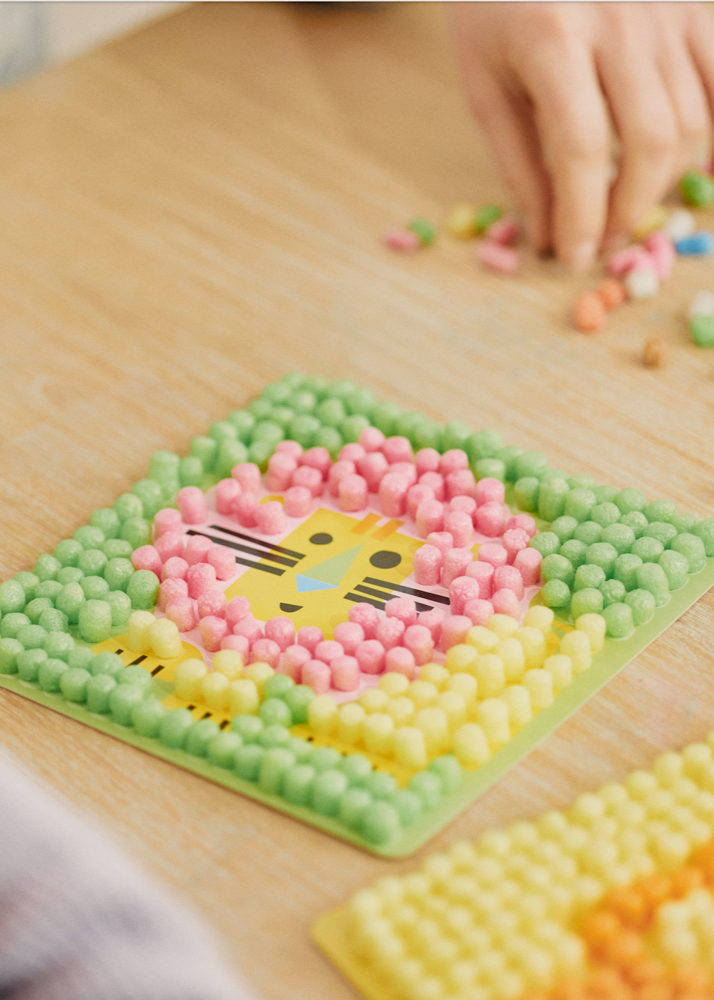 Bastelprojekt mit bunten Nubsis auf einer Tafel, die ein Tiergesicht bildet. Eine Hand sortiert weitere Nubsis daneben.