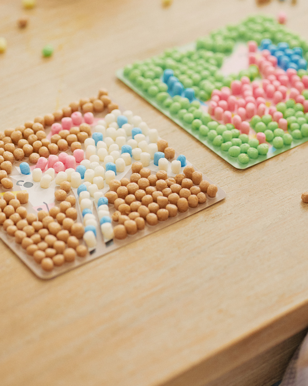 Zwei quadratische Karten mit bunten nubsis-Mosaiken auf einem Holztisch.