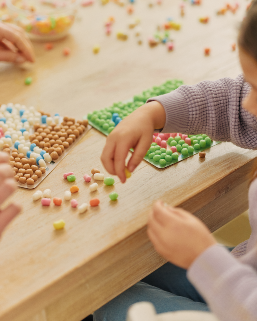 Kind bastelt mit bunten Nubsis-Bausteinen auf einem Tisch, umgeben von verschiedenen Mustern auf Matten.