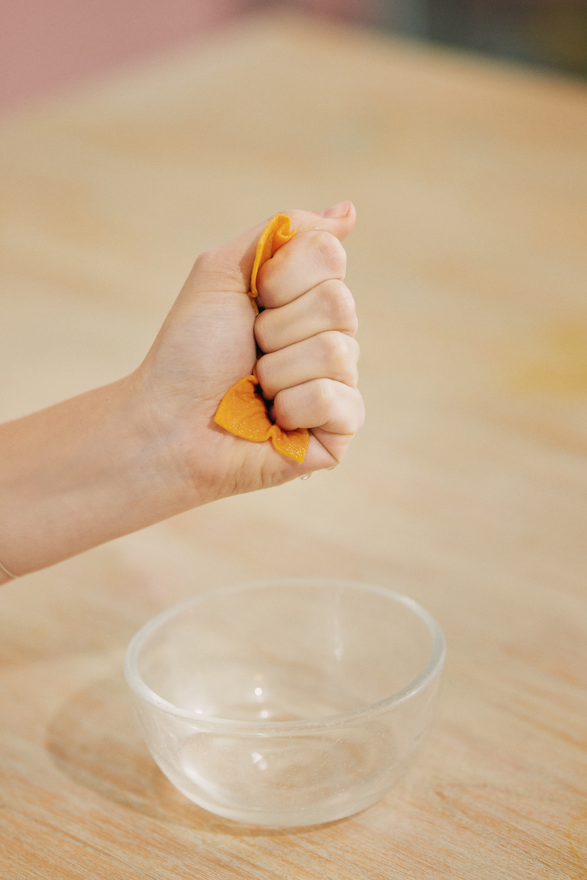 Eine Hand, die ein orangefarbenes Tuch über einer leeren Glasschüssel auspresst.