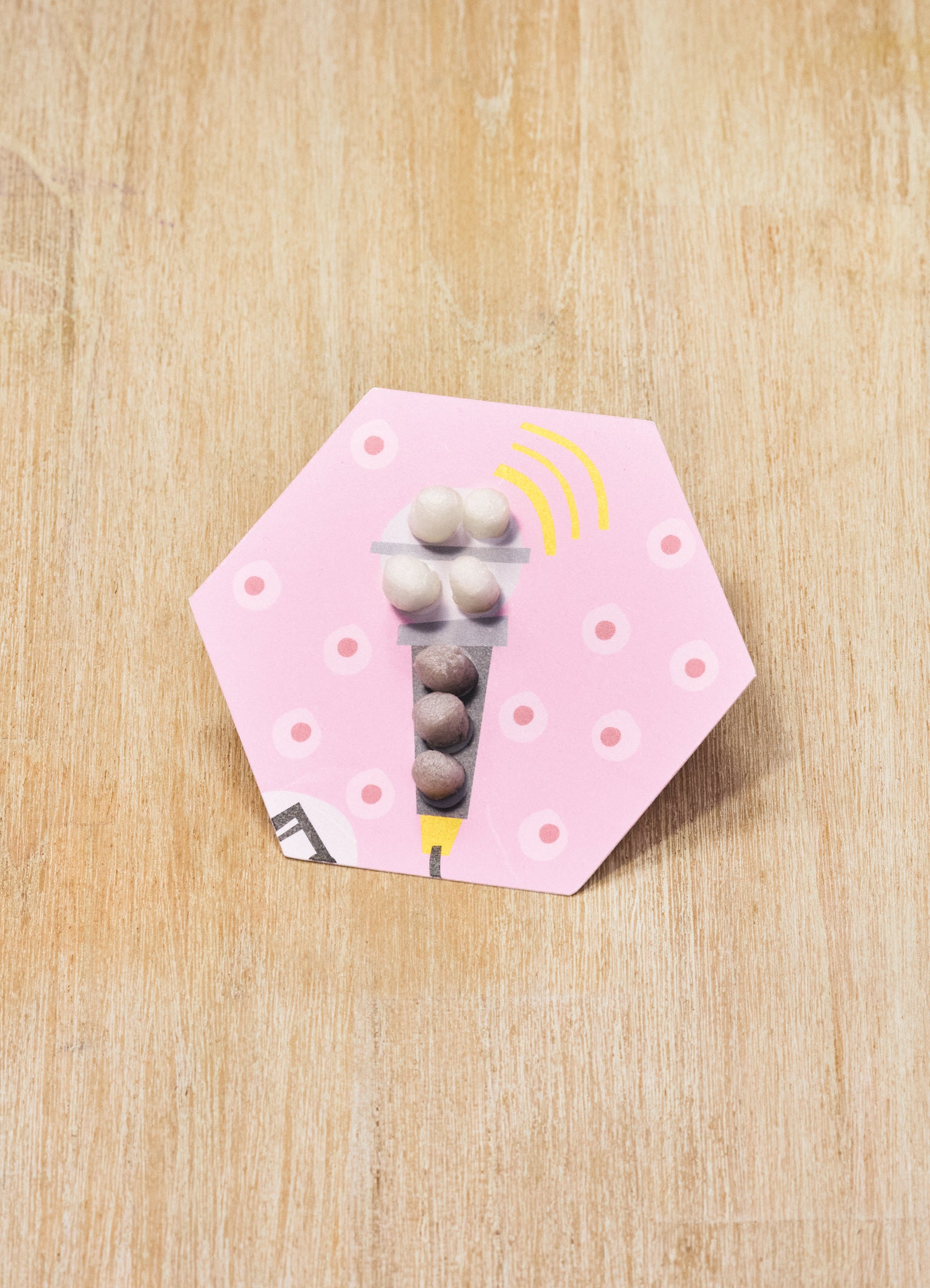 Sechseckige pinke Karte mit Mikrofonmotiv und bunten Nubsis darauf, auf Holzoberfläche liegend.