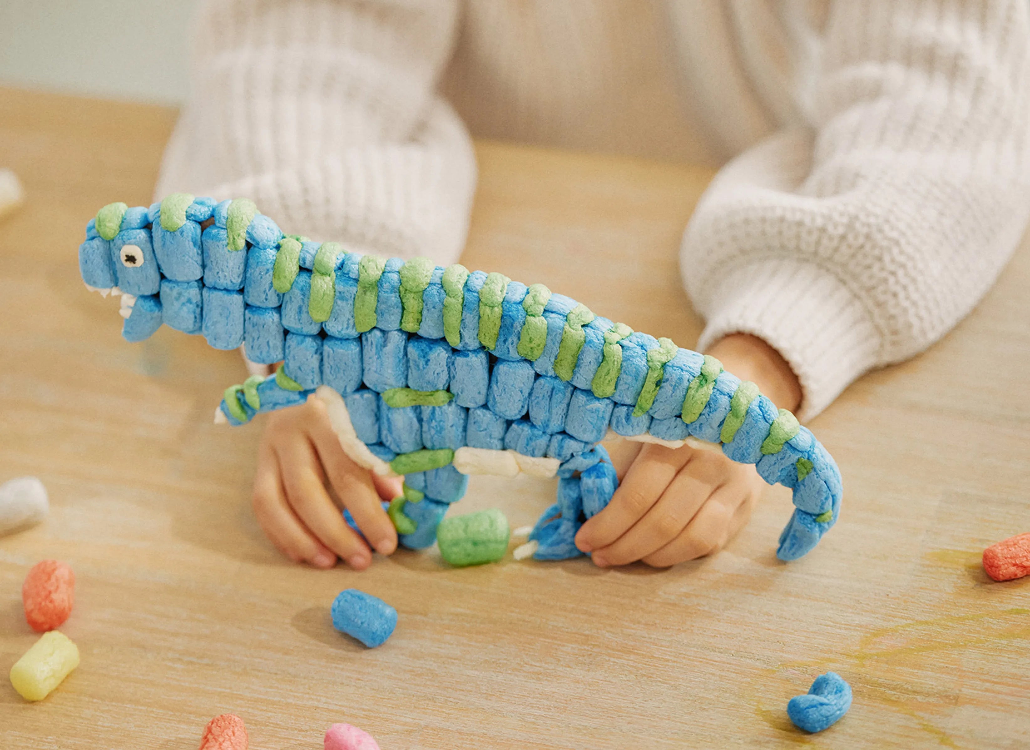 Ein Kind hält einen aus blauen und grünen Nubsis gebauten Dinosaurier.