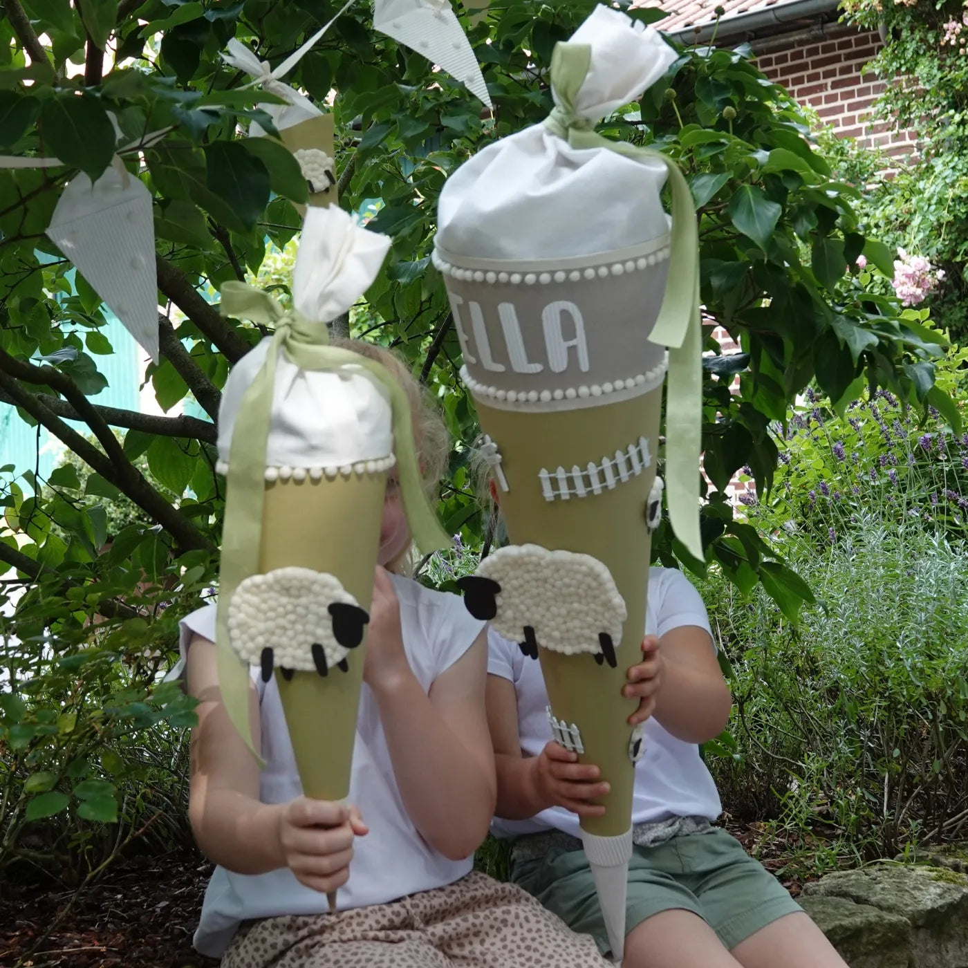 Zwei Kinder mit Schultüten, die mit Playmais dekoriert sind. Über ihnen hängt eine Wimpelkette, die ebenfalls mit Playmais dekoriert ist. Die Farbwelt ist hellgrün und weiß.