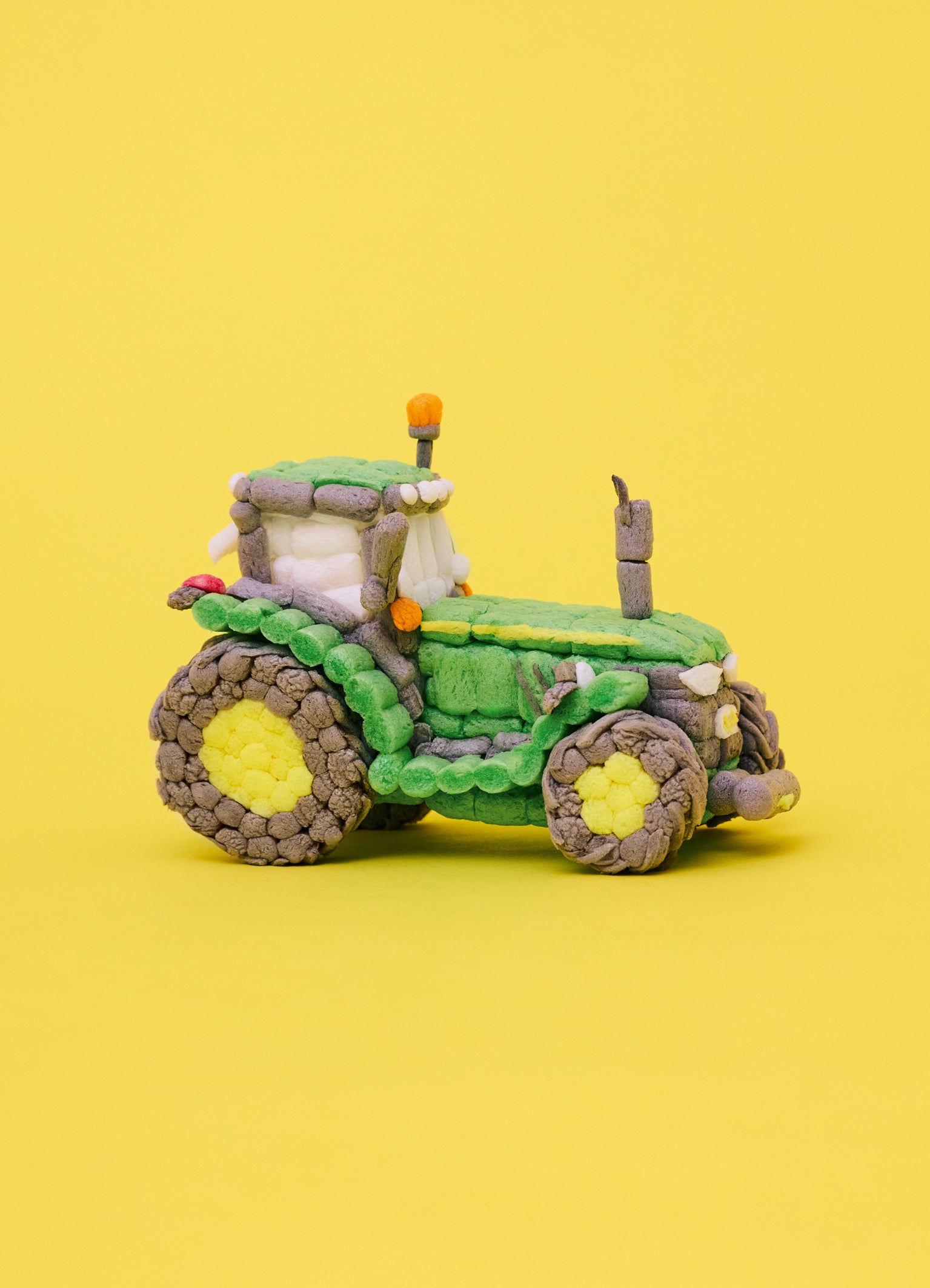 Ein Traktor aus Playmais Classic-Teilen. Hauptsächlich in den Farben Grün, Gelb und Braun. Vor gelbem Hintergrund.